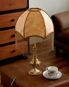 a table lamp sitting on top of a wooden table next to a cup and saucer