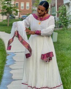 a woman in a white dress is standing on the sidewalk and looking down at her hand