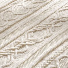 the white knitted blanket is laying on top of the bed coverlet with an intricate design