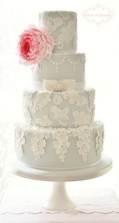 a three tiered wedding cake with white lace and pink flower on the top layer