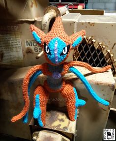 an orange and blue crocheted stuffed animal sitting on top of a metal object