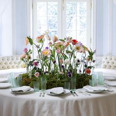 an arrangement of flowers in glass vases on a table with plates and utensils