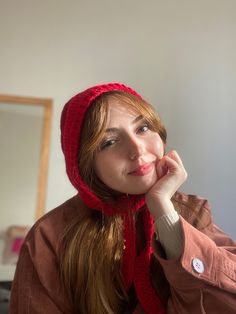 a woman wearing a red hat and scarf with her hand on her chin looking at the camera