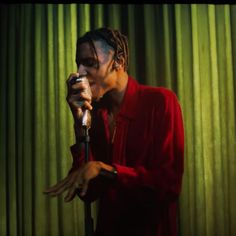 a man with dreadlocks holding a microphone in front of green curtained background