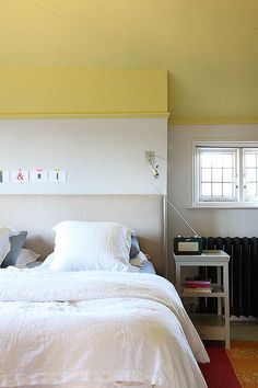 a white bed sitting under a window next to a table with a lamp on it