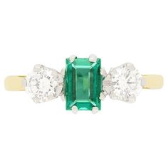 This classic Vintage trilogy ring dates to the 1980s and features a captivating 0.50 carat baguette-cut emerald at its centre, radiating with rich green hues. Flanking the emerald are two round brilliant cut diamonds, each weighing 0.25 carats. Each diamond is of exceptional quality, matching at F in colour and VS1 in clarity. The trio of stones are claw set into platinum collets with a contrasting band of 18 carat yellow gold band completing the ring beautifully. Gemstone: Emerald Stone Shape: Baguette Cut Carat Weight: 0.50 Metal: 18ct White Gold, 18ct Yellow Gold Age: 1980s Size: N Heart Shaped Diamond Ring, Carved Ring, Three Stone Ring, Three Stone Engagement, Heart Shaped Diamond, Stone Engagement Rings, Platinum Ring, Three Stone Rings, Yellow Diamond