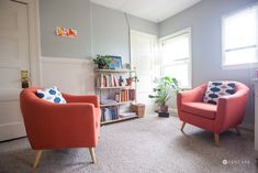 two orange chairs sitting in a living room next to a book shelf