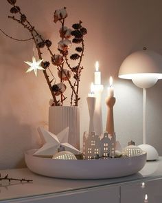 a white bowl with some candles in it on top of a table next to a vase