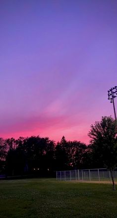 the sky is pink and purple as the sun goes down over a soccer field with trees in the background