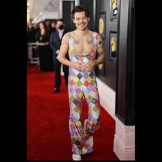 a man with tattoos standing in front of a red carpet wearing colorful pants and a tank top