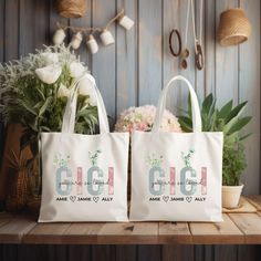 two white bags sitting on top of a wooden table next to flowers and potted plants