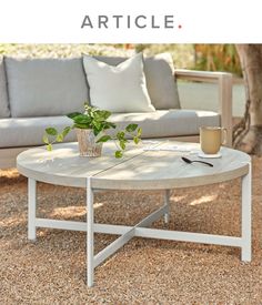 a coffee table sitting on top of a gravel ground next to a couch and tree