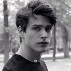 a black and white photo of a young man looking at the camera with trees in the background