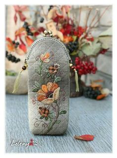 an embroidered purse with flowers on it sitting on a table next to berries and leaves