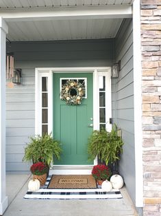 a green front door with two potted plants and a wreath on the entrance mat