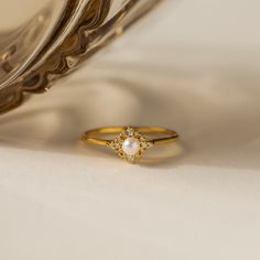 a close up of a gold ring with a pearl on the side and a silver plate in the background