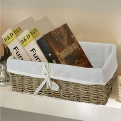 a basket filled with books on top of a white shelf next to a bottle of wine