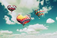 three hot air balloons flying in the sky with some clouds behind them and one heart shaped balloon