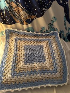 a crocheted blue and white blanket sitting on top of a bed next to a pillow