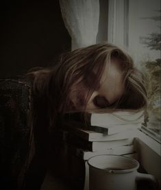 a woman leaning over a stack of books with her head on top of a coffee mug