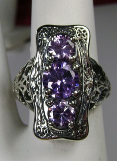 "Purple Amethyst Cubic Zirconia Description 3Stone Rectangle Design#60 MADE TO ORDER This is a lovely Edwardian reproduction 3 gemstone ring in solid sterling silver. The gorgeous filigree ring is set with 3 round cut purple amethyst CZ. The 2 smaller amethyst CZ's are 4.5mm in diameter; and the center amethyst CZ is 6mm in diameter. This filigree setting is a cast from an actual Antique design; notice the amazing etched accents... The ring sits 3/4th\" (19mm) NS on the finger. The quality of th Antique Silver Three Stone Jewelry, Unique Silver Three-stone Jewelry, Ornate Silver Amethyst Ring For Anniversary, Ornate Purple Ring For Anniversary, Purple Ring With Intricate Design, Ornate Purple Amethyst Ring, Unique Silver Three Stone Jewelry, Unique Silver Jewelry With Three Stones, Antique Three Stone Jewelry Gift