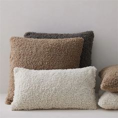 four pillows stacked on top of each other in different colors and sizes, one is brown, the other is white