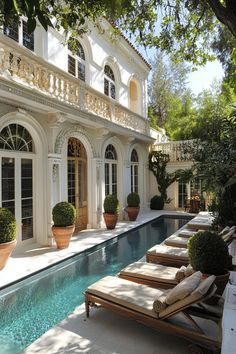 an outdoor swimming pool with lounge chairs and potted trees in front of the house