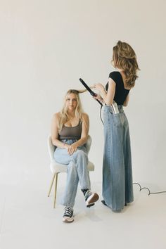 a woman sitting in a chair while another person blow dries her hair with an iron