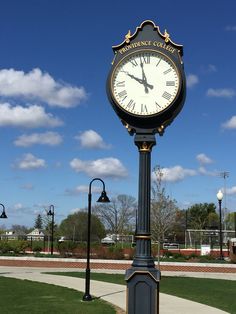 a large clock on top of a pole in the middle of a grass covered park