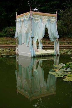 a bed sitting on top of a lake next to a lush green forest filled with water lilies