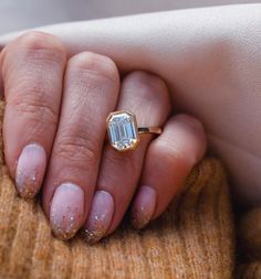 a woman's hand holding an engagement ring with a green diamond on the middle