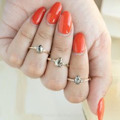 a woman's hand with three rings on her fingers and an orange manicure