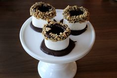 four desserts on a white plate with chocolate and nuts in the middle, sitting on top of each other