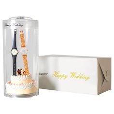 a watch in a glass case next to a box with the word happy wedding written on it