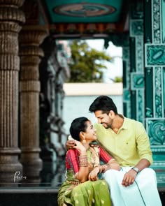 a man and woman sitting next to each other in front of an ornate building with columns