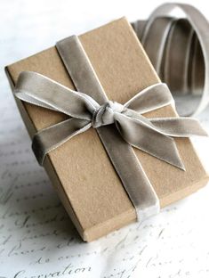 a brown box with a silver ribbon tied around it and sitting on top of a piece of paper