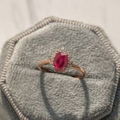 a ring with a red stone in it on top of a gray cloth covered box