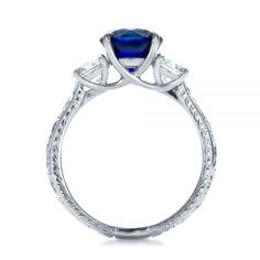 100603 Platinum Ring   2 Diamonds - .83 ctw   Clarity: VS2 - Color: F-G. This elegant engagement ring features a round blue sapphire, flanked on either side by a smaller round diamond, all atop a platinum shank with custom hand-engraved accents. It was created for a client from Woodinville, WA, and it can be modified in several different ways to make it match your personal style.       To begin the custom design process, you’re welcome to come visit our Bellevue, WA showroom personally. However, Blue Three Stone Sapphire Promise Ring, Blue Sapphire Three-stone Promise Ring, Blue Three Stone Diamond Ring, Sapphire Three Stone Round Cut Diamond Ring, Blue Three Stone Round Cut Diamond Ring, Three Stone Lab-created Sapphire Diamond Ring, Three Stone Sapphire Diamond Ring With Round Cut, Blue Three Stone Sapphire Ring, Trillion Cut Sapphire Ring With Center Stone