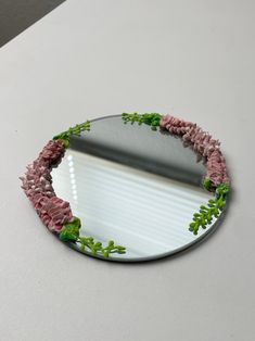 a mirror with flowers on it sitting on top of a white table next to a wall