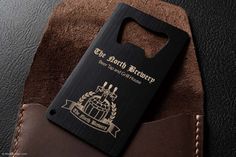 a black and brown wallet with a bottle opener on it's back pocket that has a leather label attached to it