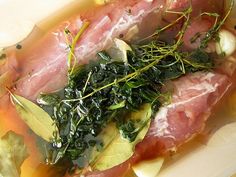 some meat and greens are in a bowl on a table with lemons, water, and other ingredients