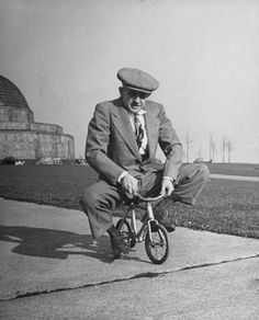 an old man in a suit and tie riding a bike