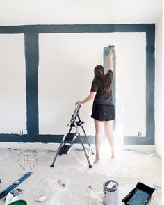 a woman standing on a ladder painting the walls