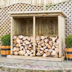 a wooden shed filled with logs next to two planters and a fence in the background