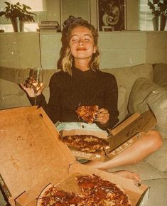 two women sitting on a couch holding pizzas and wine glasses in front of them