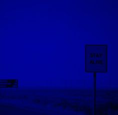 a street sign sitting on the side of a road next to a blue sky at night