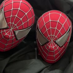 two red masks sitting on top of a black cloth covered bedding with spiderman's face