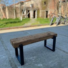 a wooden bench sitting on top of a cement floor next to a building with windows