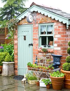 a small brick building with potted plants and a clock on the window sill