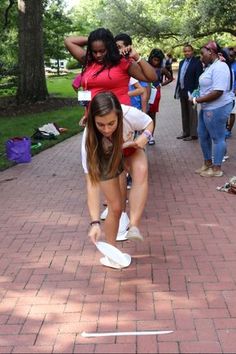 a woman is bending over to pick up a frisbee from the ground while others look on